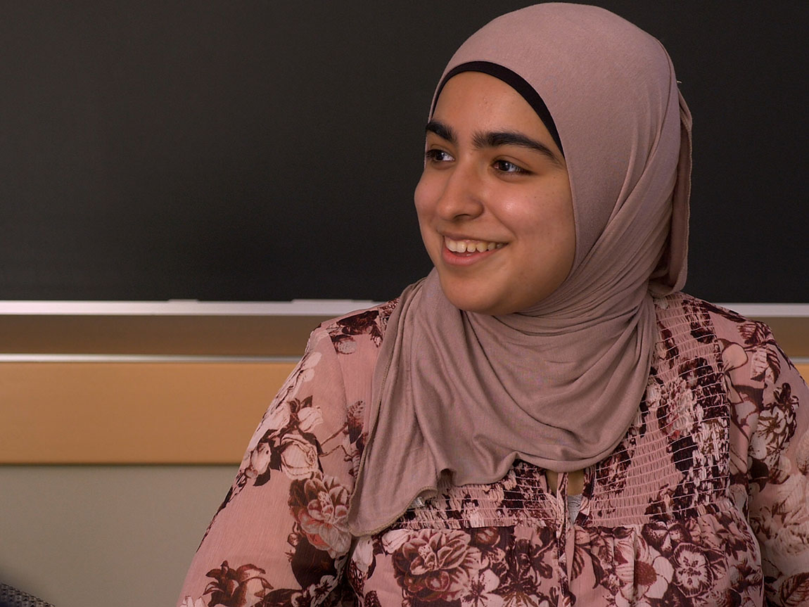 A college student in a hijab smiles in a classroom